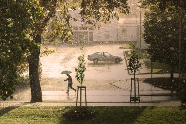 En person hukar under ett paraply när regnet vräker ned.